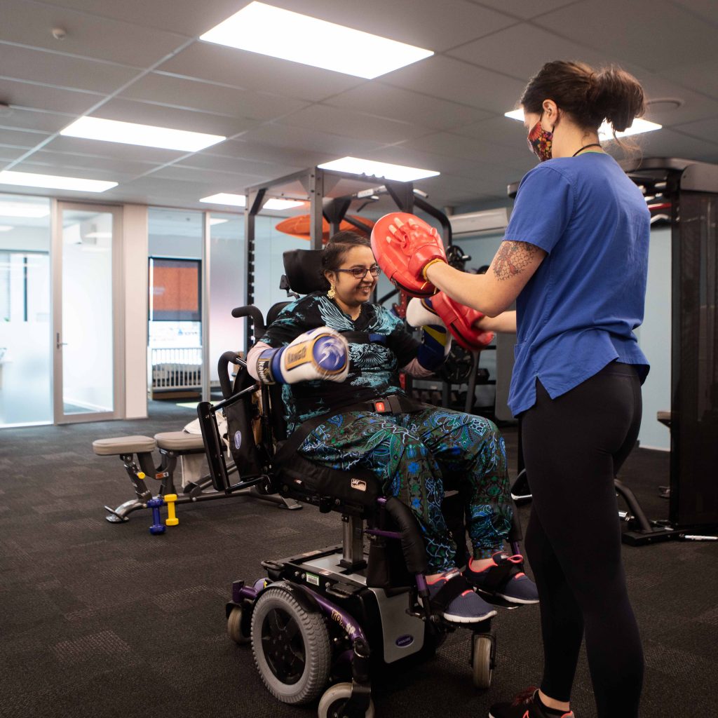 Woman in wheelchair exercises with female Physiotherapist at Phoenix Health Hub Christchurch Rehabilitation Disability Mobility Training Boxing pads